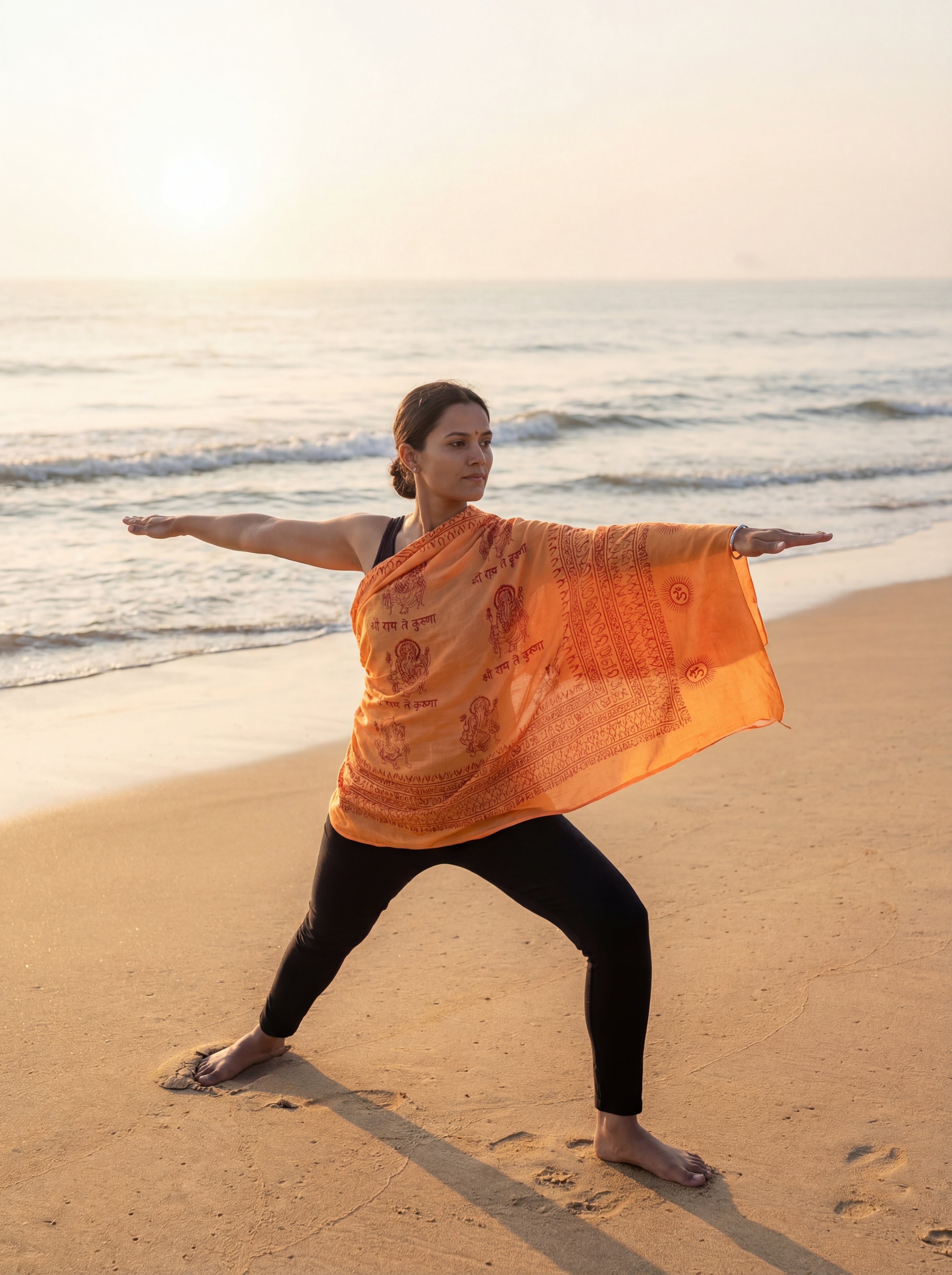 Woman practicing yoga on a beach with an orange yoga shawl hand printed with a Ganesha pattern