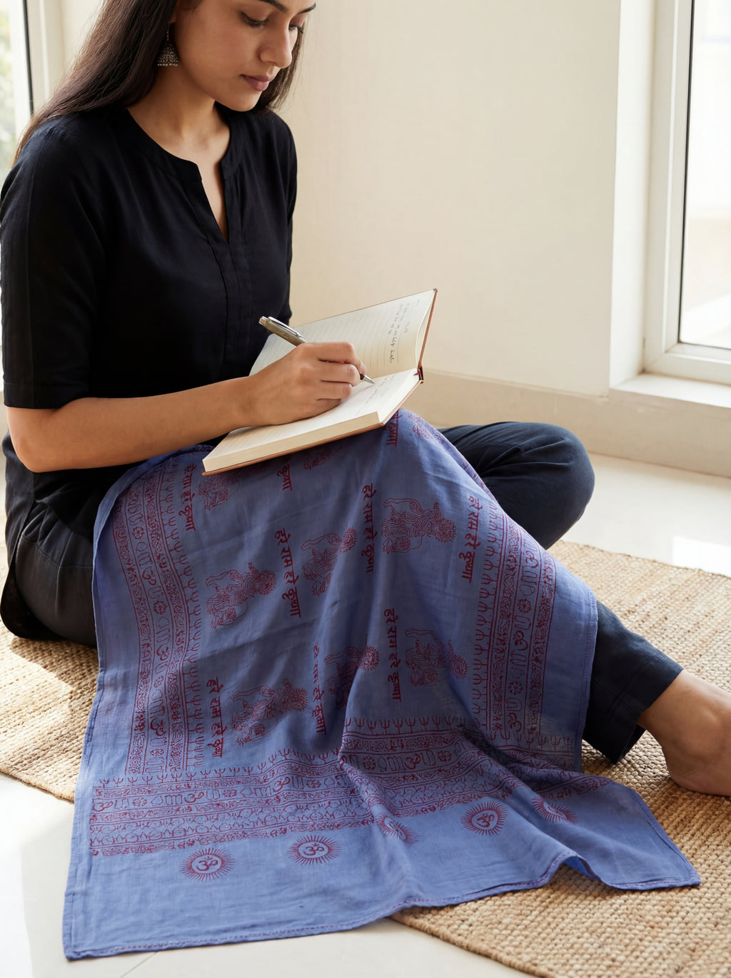 Woman sitting on the floor with a blue Krishna patterned yoga shawl, writing in a notebook.
