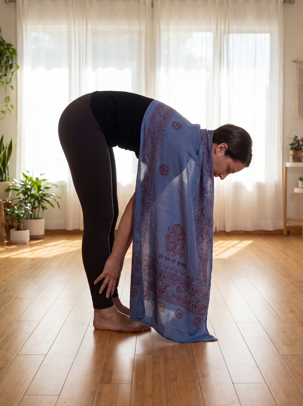 Person practicing yoga with a blue Ganesha pattern hand printed yoga shawl draped over their shoulder in a bright room with plants.