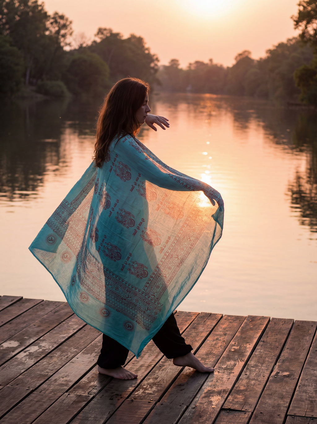 Blue Ganesha yoga shawl worn by a woman standing on a wooden dock by a lake at sunset.