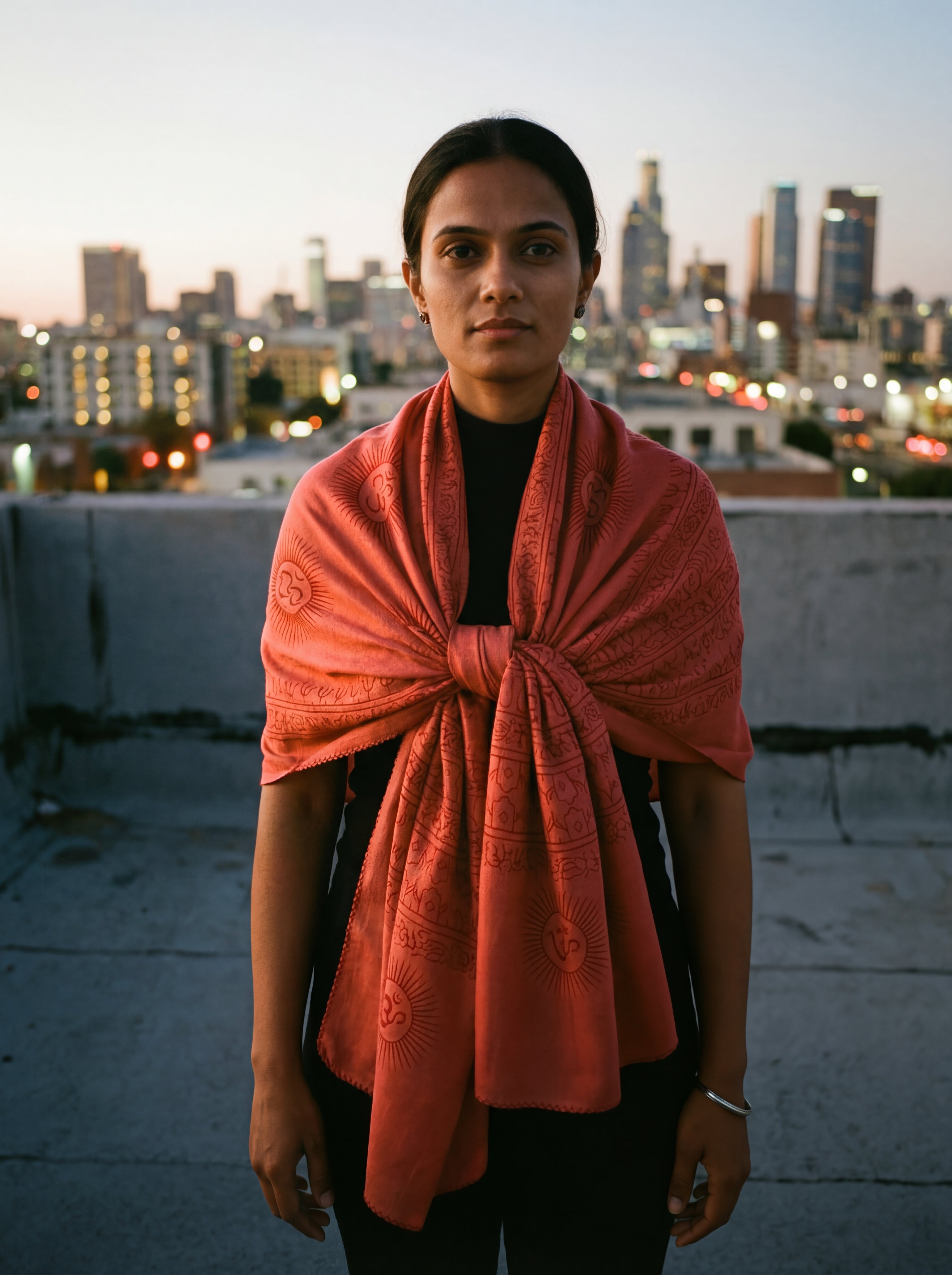 Red Om print lightweight yoga scarf wrap loosely knotted around a woman's shoulders with a city skyline in the background