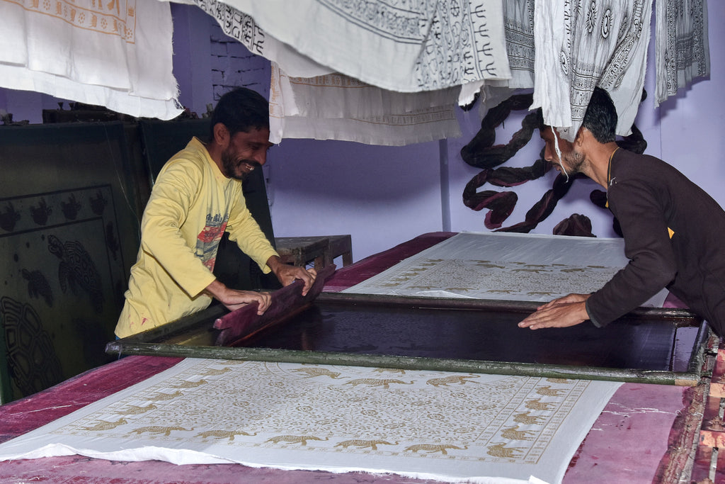 Two men using traditional silk screen printing process with fabric and the Ganesha pattern for Ram Nami Trading Co. Indian scarves.