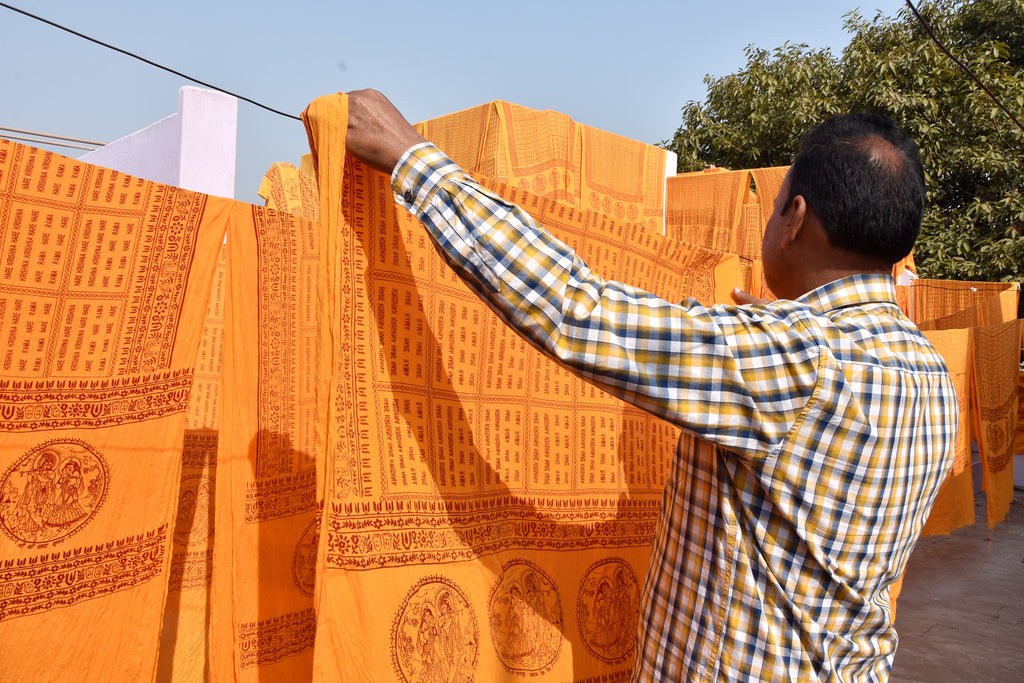 Man hanging orange yoga shawls with patterns on a line outdoors