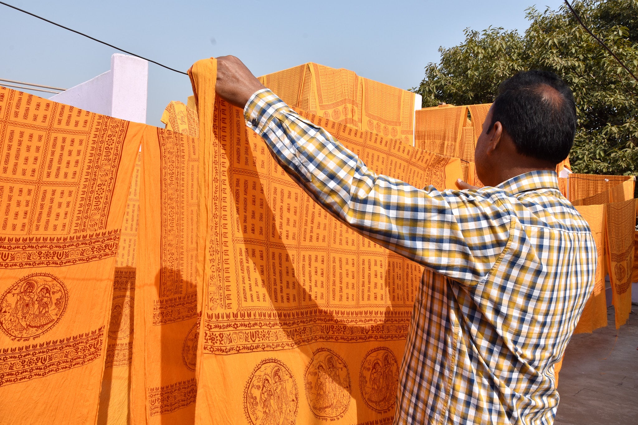 Man hanging orange yoga shawls with patterns on a line outdoors