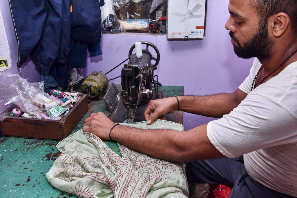 Man working on a sewing machine to make the Ram Nami Trading Co Yoga Scarves